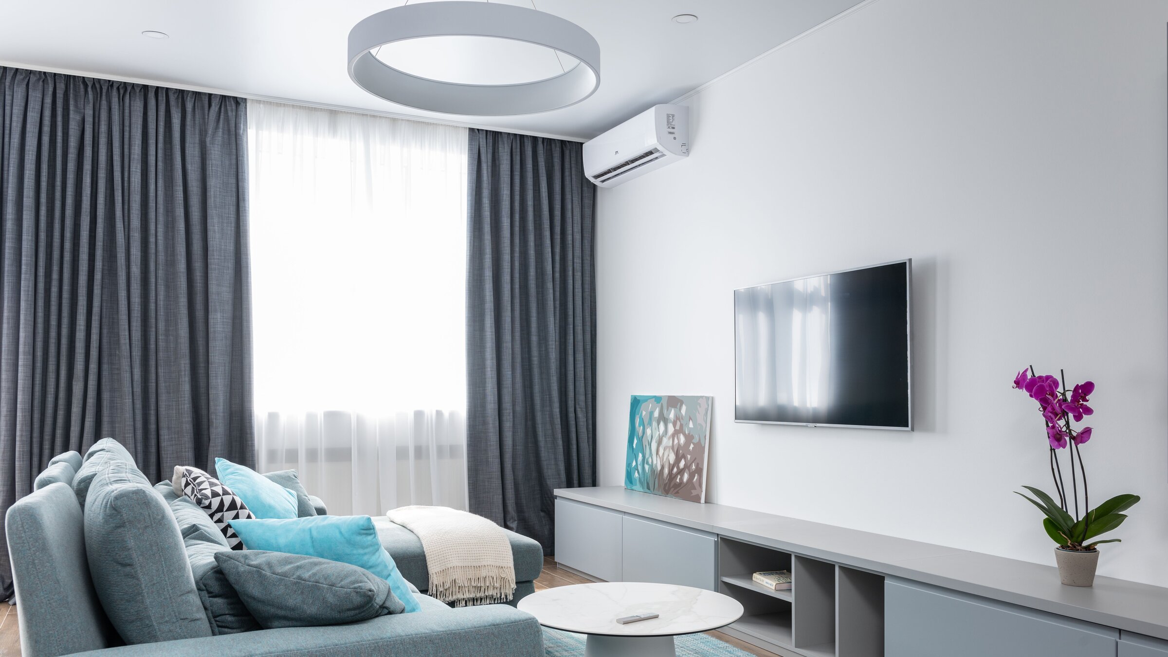 Bright modern living room with a clear white wall-mounted air-conditioner above the sofa — calm cooled domestic interior