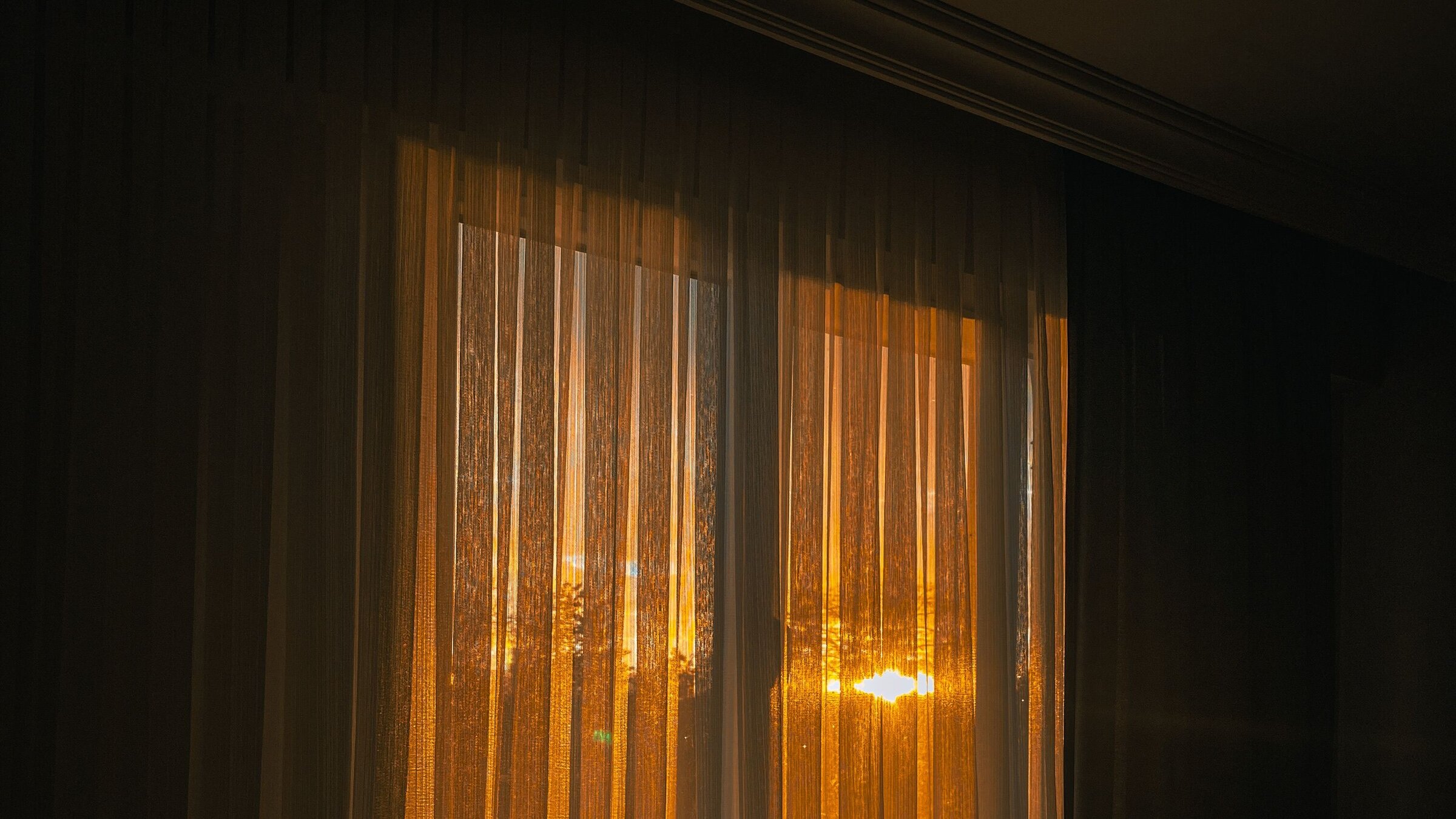 Intense golden sunset blazing through sheer curtains into a darkened domestic room — clear heat-wave light