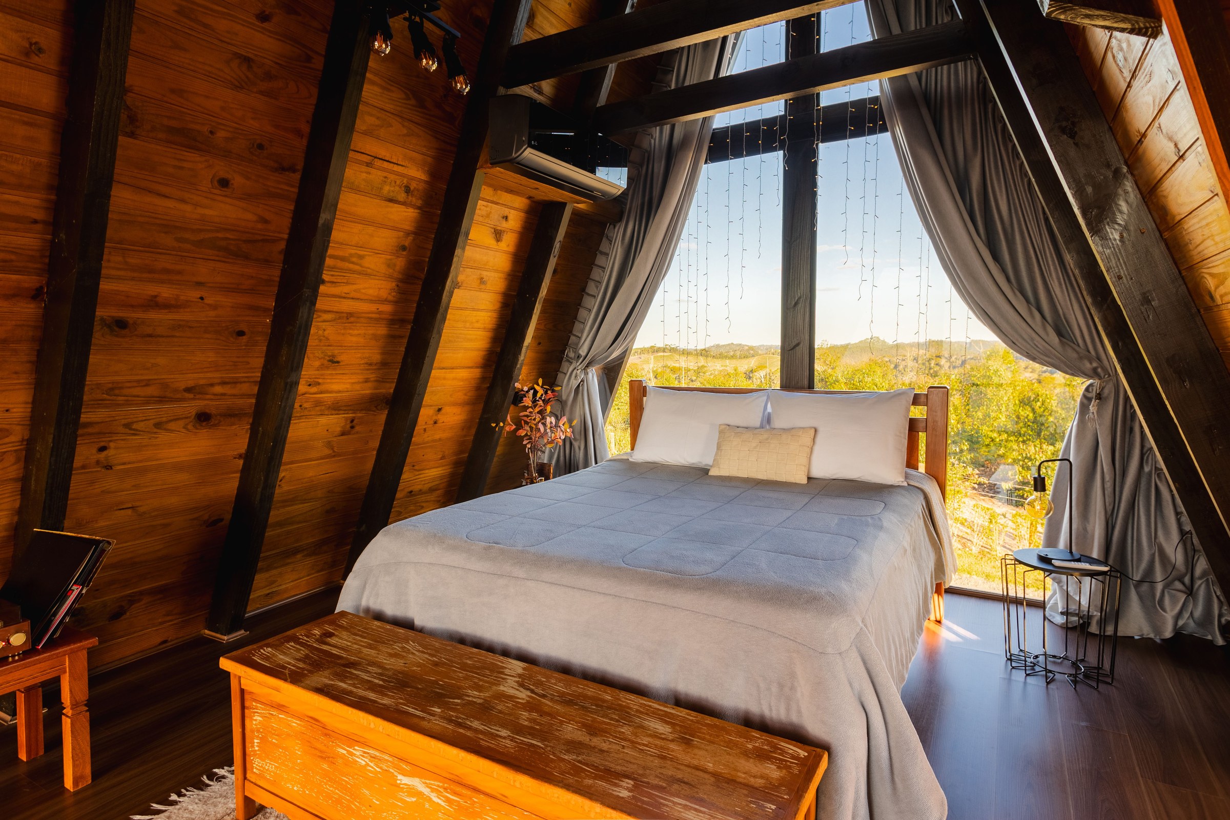 Black wall-mounted split air-conditioner in a timber bedroom with warm afternoon light through a large window